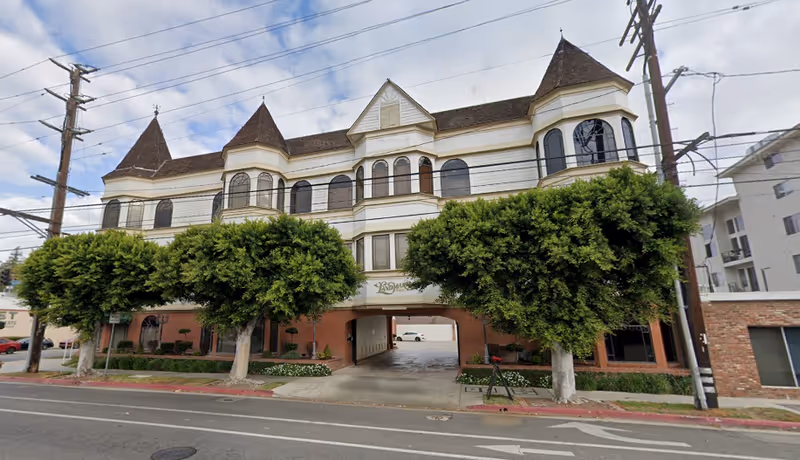 Three-story building with arched windows, towered roofs, and a central archway entrance.