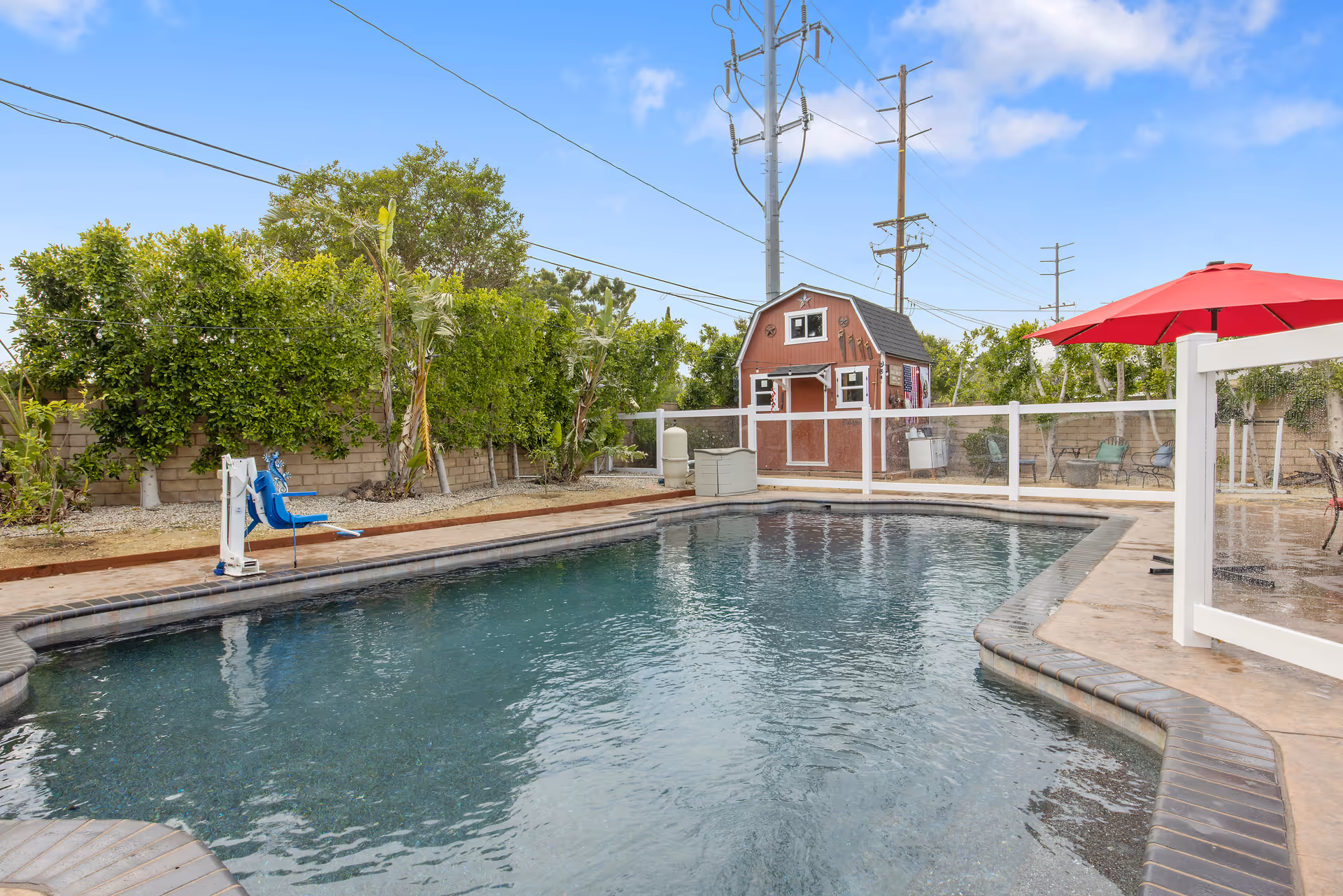 Outdoor pool area with a fenced pool, seating, and a red umbrella.