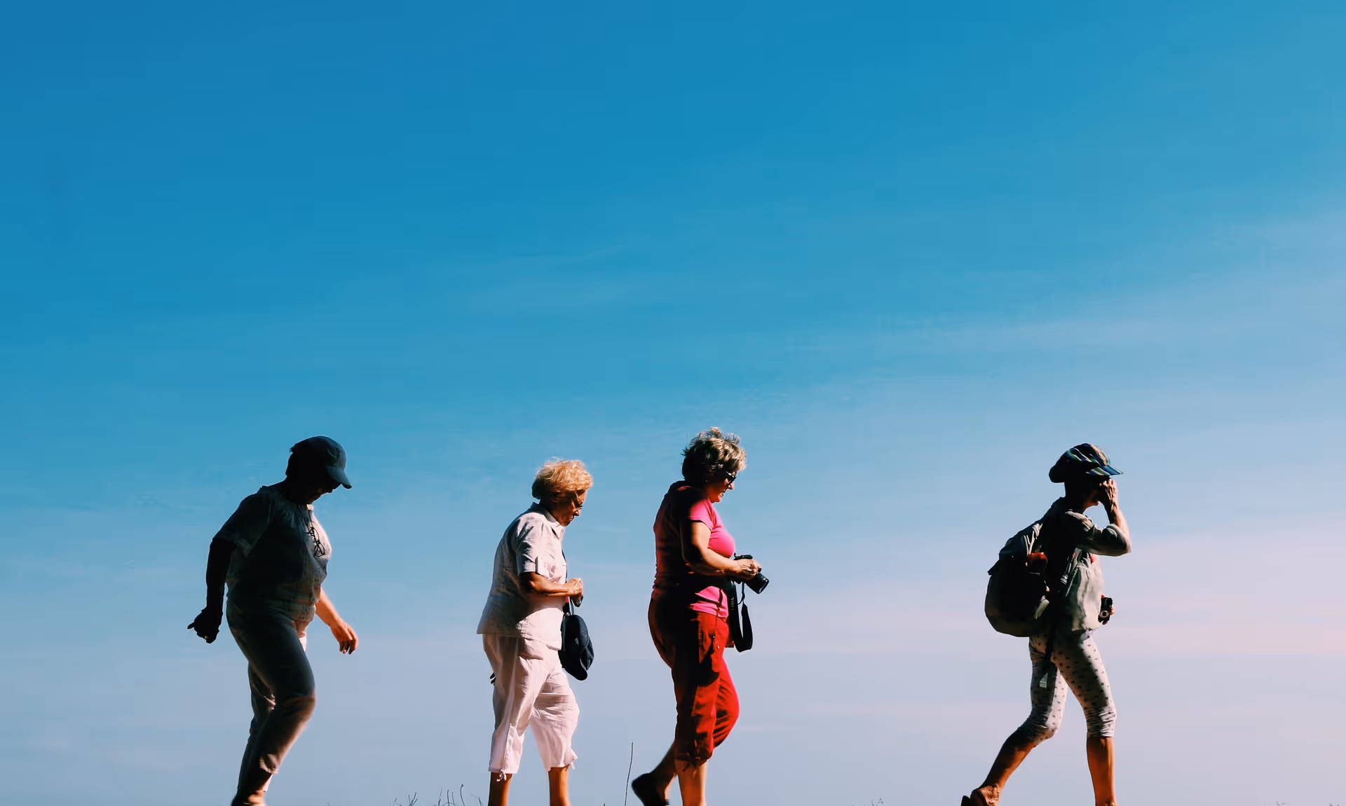 Four older adults walk outdoors under a clear blue sky.