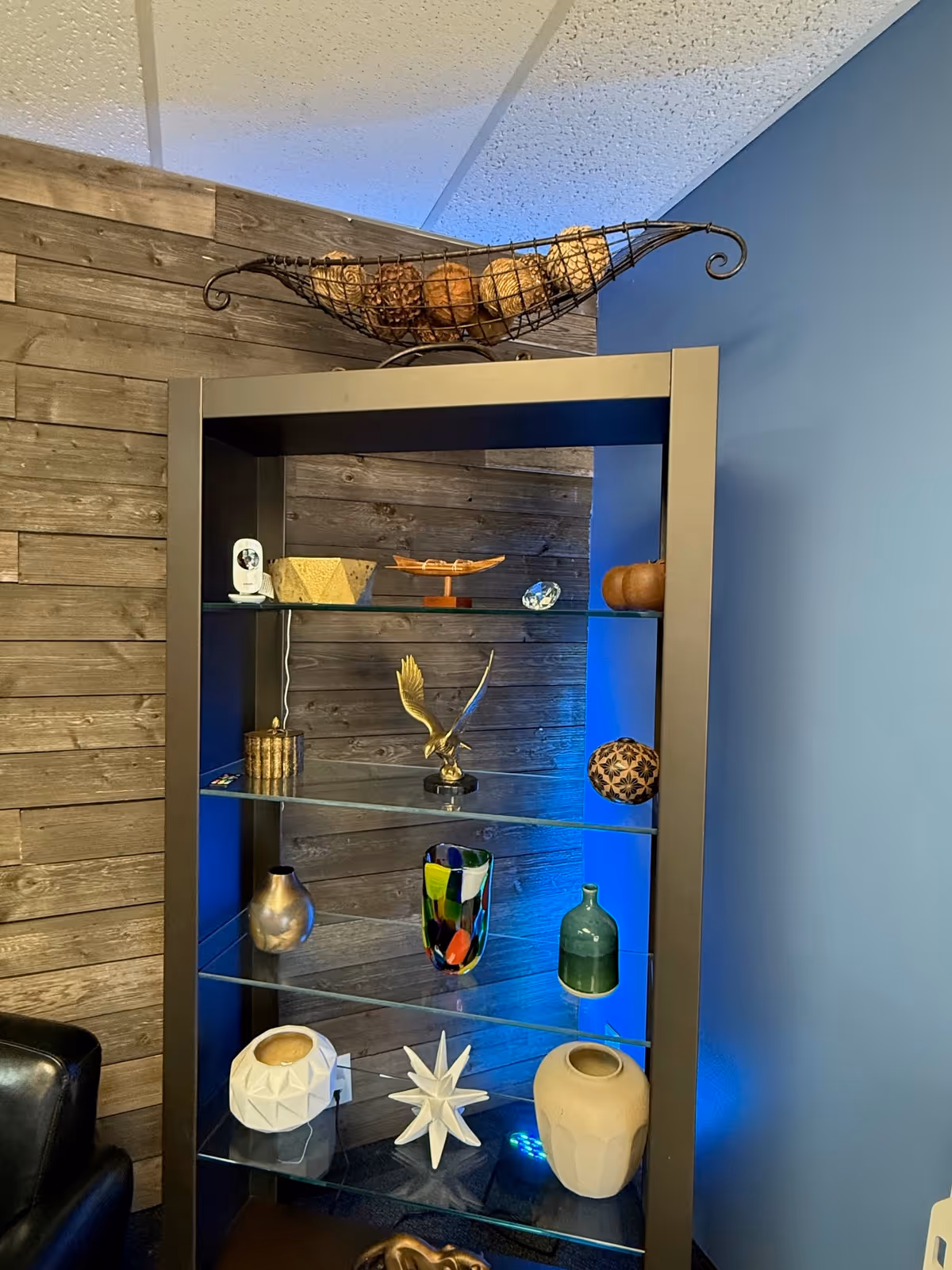 Interior display cabinet showcasing decorative pottery against blue wall and wood paneling.