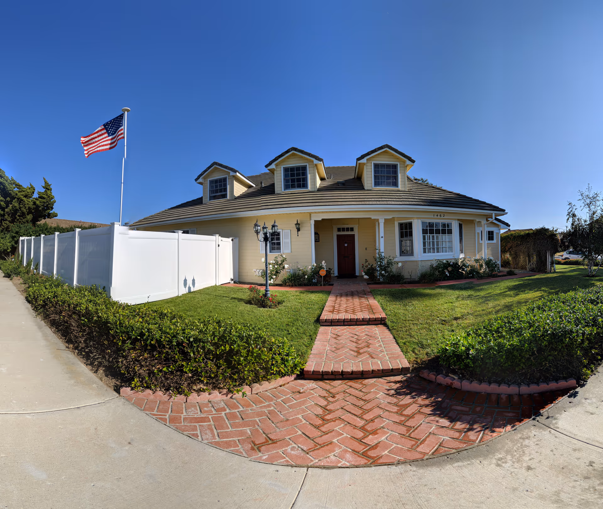 Front view of a beige, two-story building with brick path, white fence, and American flag.