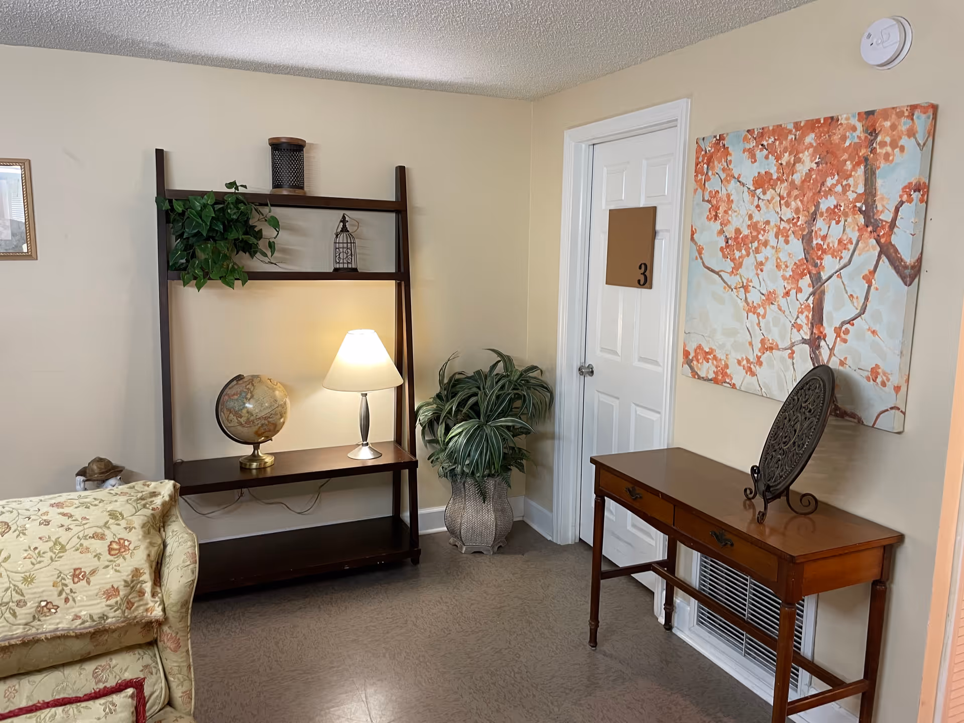Cozy living room corner with a bookshelf, lamp, plants, and wall art.