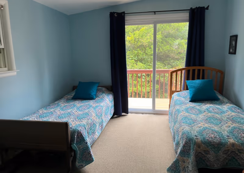 Two twin beds with turquoise bedding in a blue bedroom with sliding balcony door.
