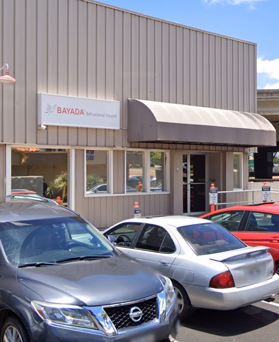 Front exterior of BAYADA Behavioral Health building with a curved awning and parked cars.