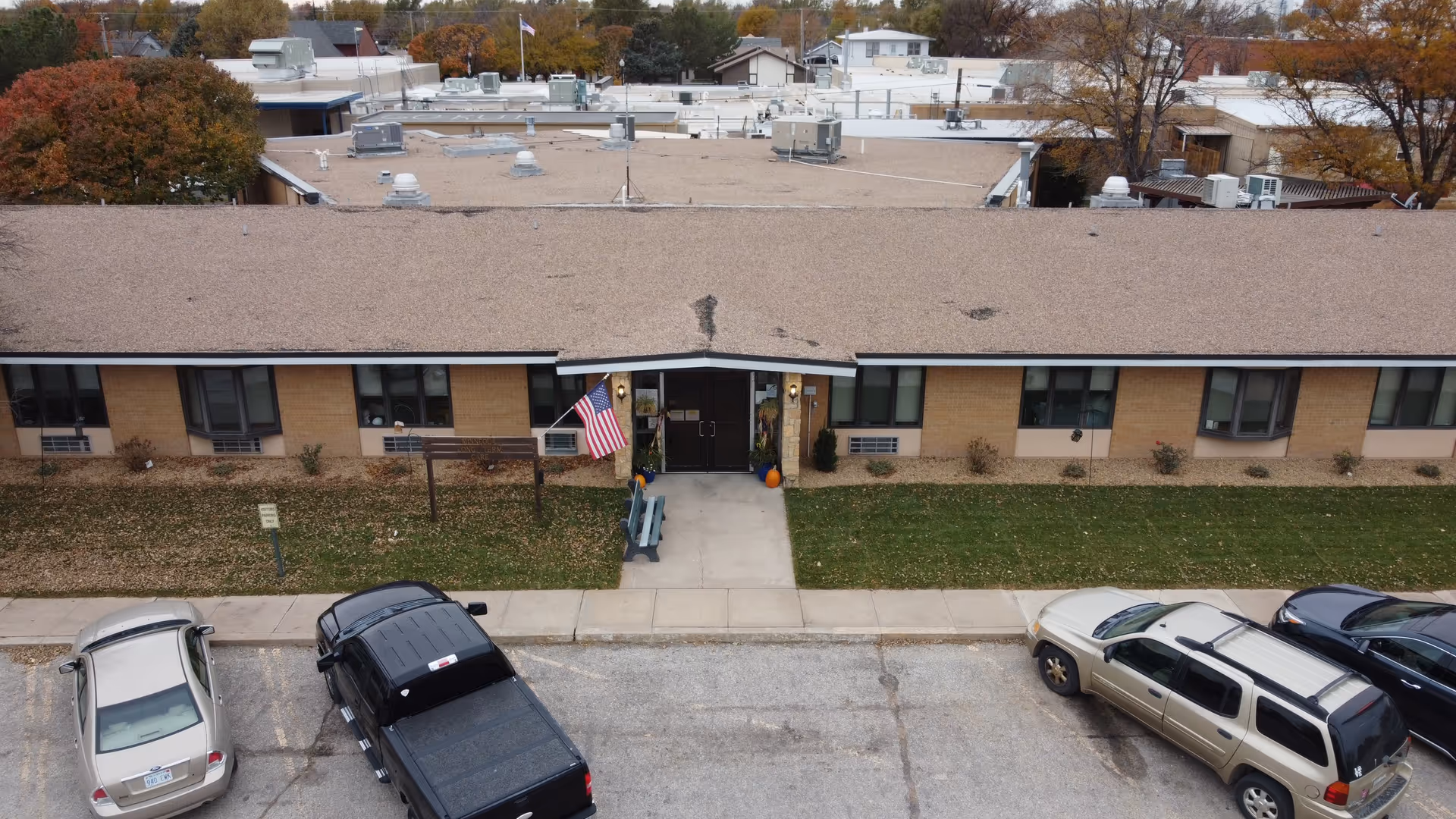 Exterior view of a single-story brick senior facility with a central entrance and parked cars.