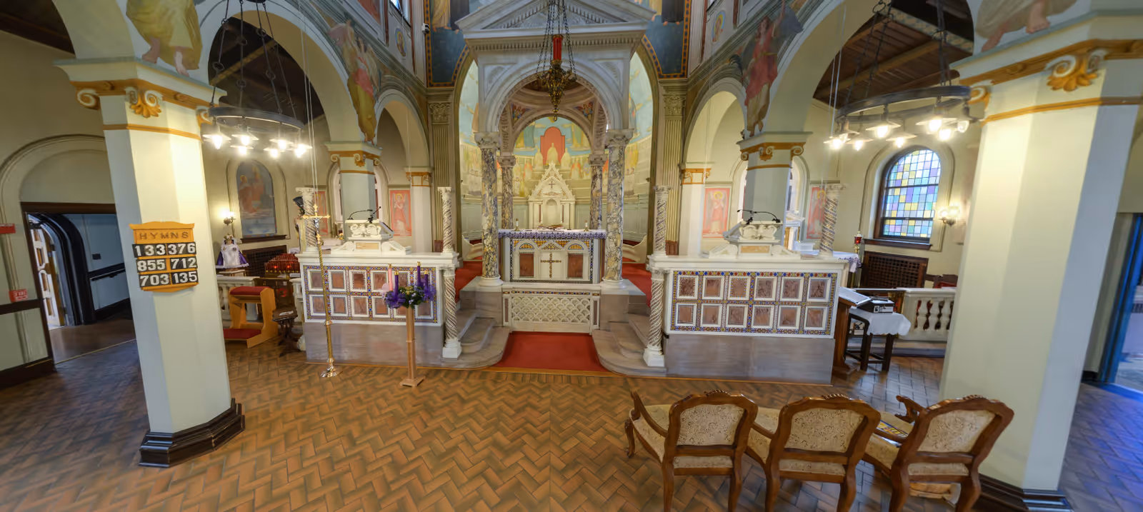Ornate chapel interior with arches, decorated altar, and rows of wooden pews.