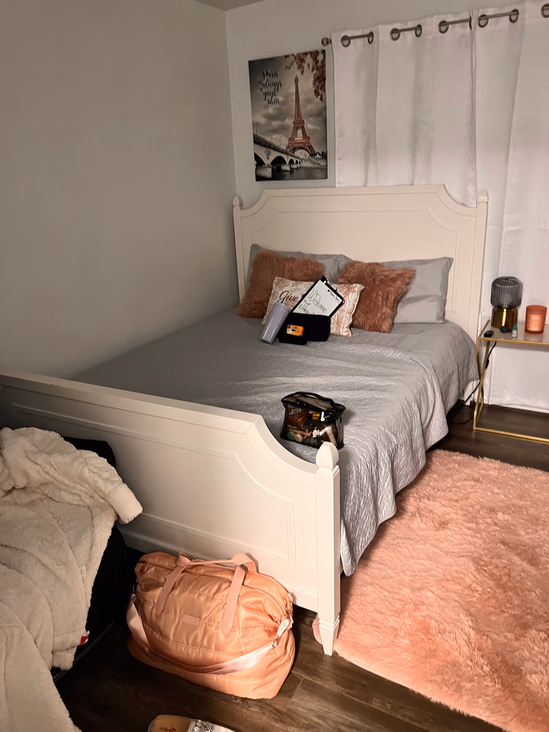White wooden bed with gray bedding in a cozy bedroom, pink rug, and nightstand.