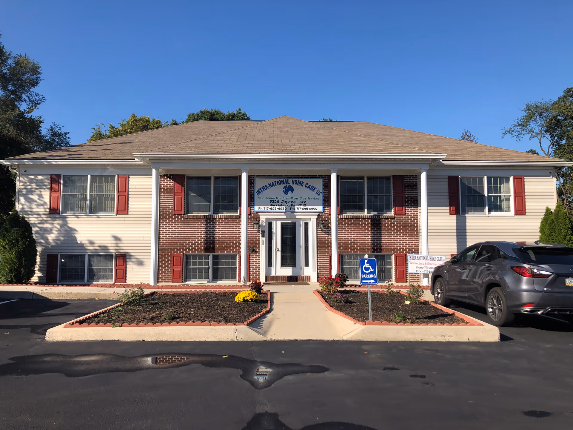 Front view of a beige-brick senior care facility with red shutters and a parking lot.