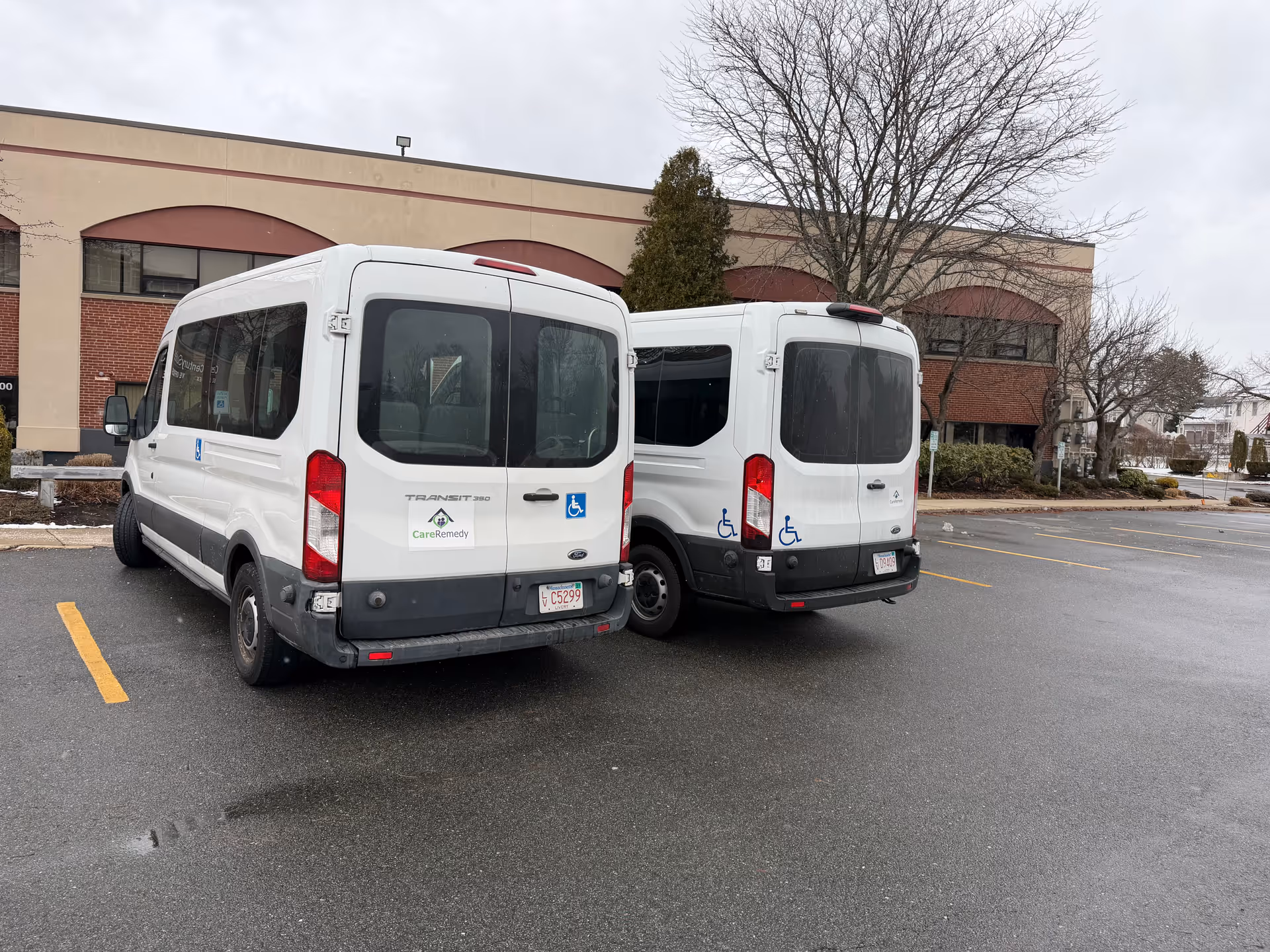Two white shuttle vans parked in a lot beside a brick building.