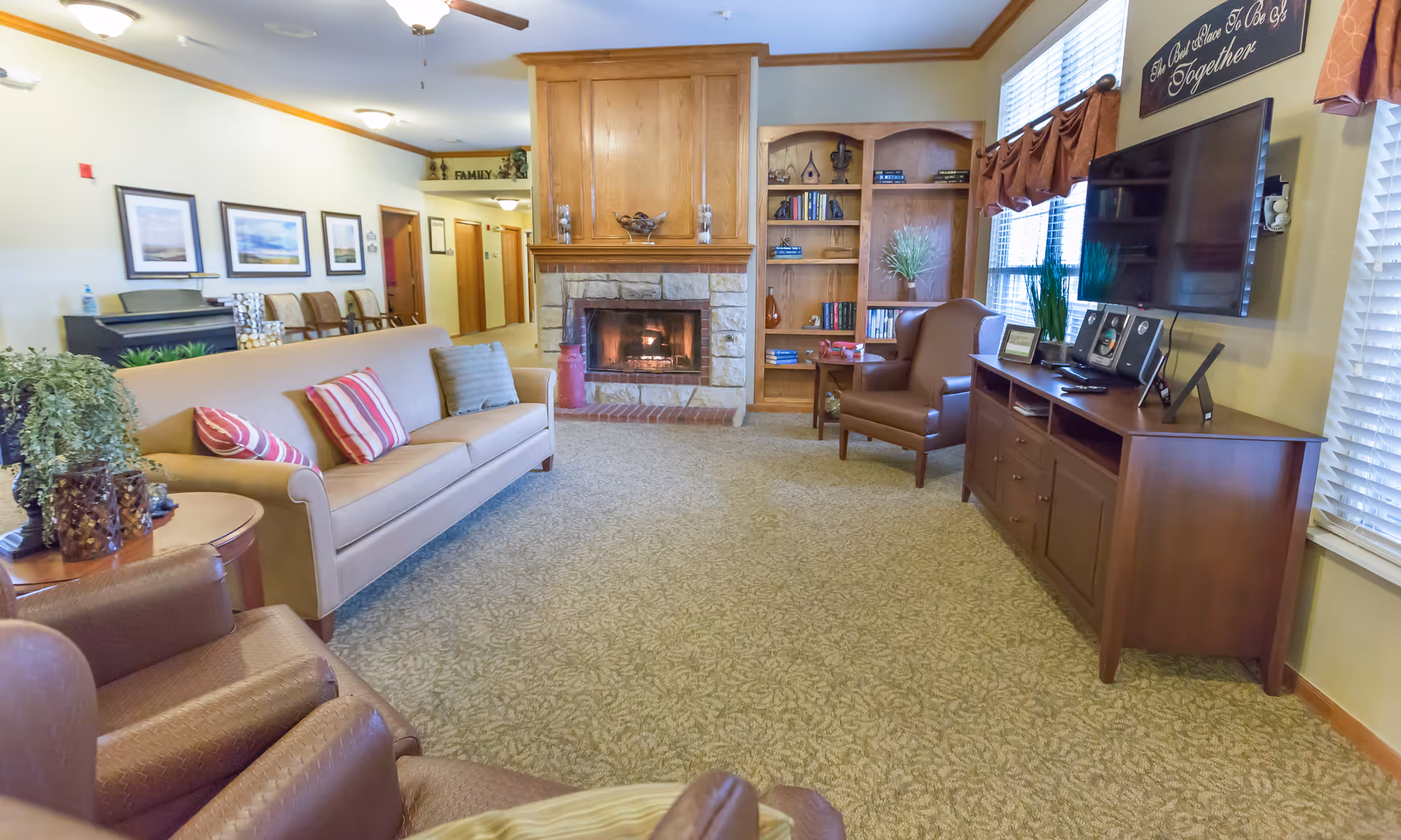 Cozy living room in a senior facility with sofa, armchairs, fireplace, and TV.