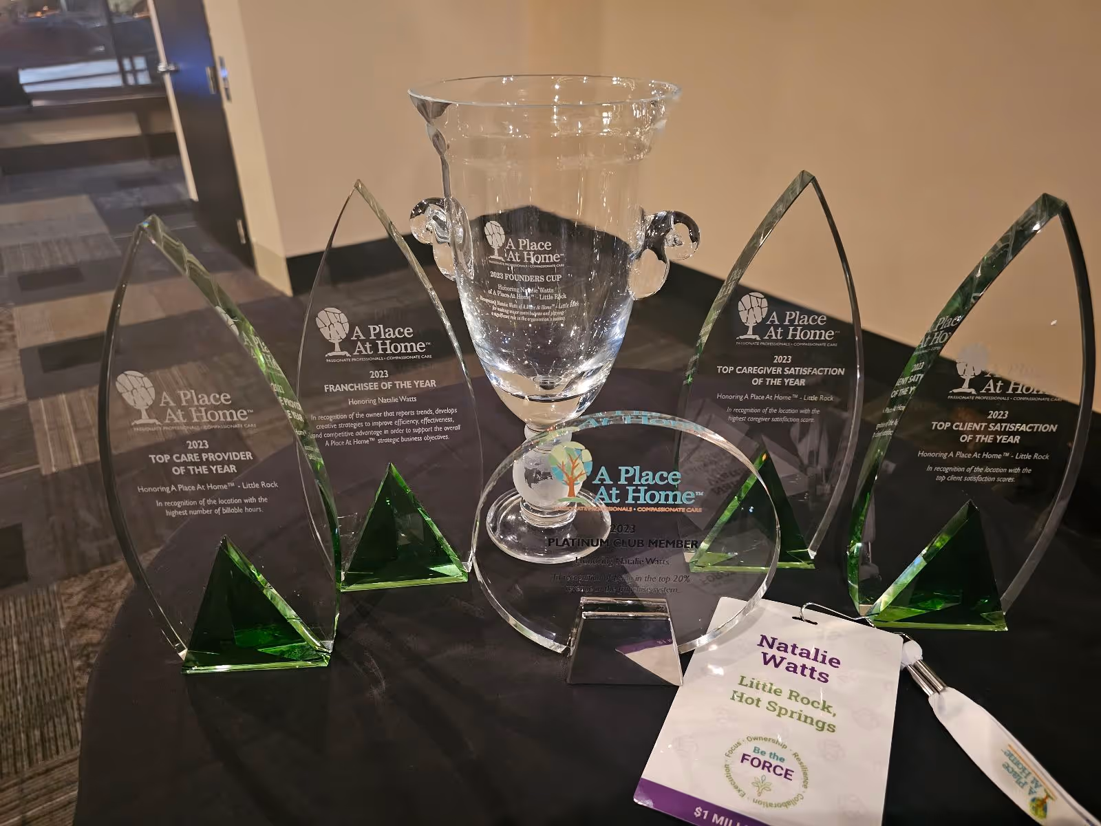 Multiple glass trophies and a brochure on a round black table indoors.