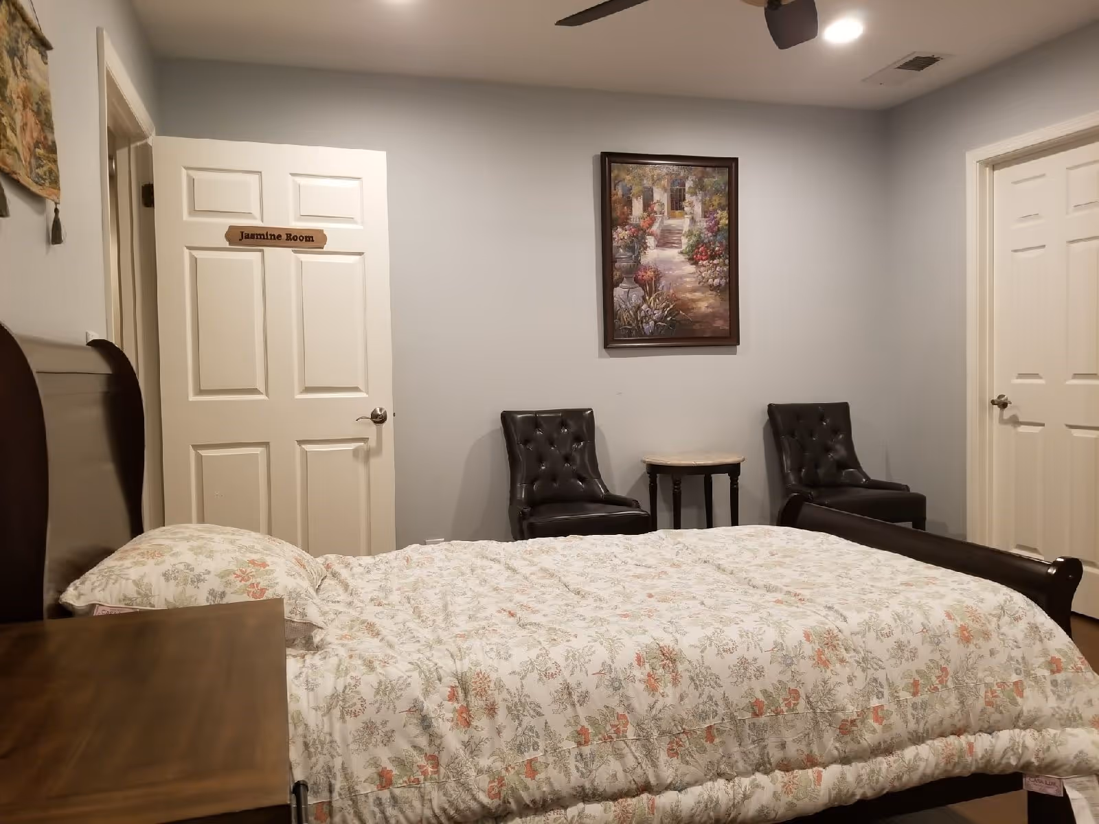 Bedroom in Rose Senior Care #2 featuring bed, chairs, table, and wall art.