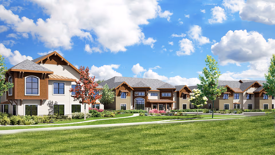 Front exterior view of a two-story assisted living building with landscaped lawns, trees, and a bright blue sky.