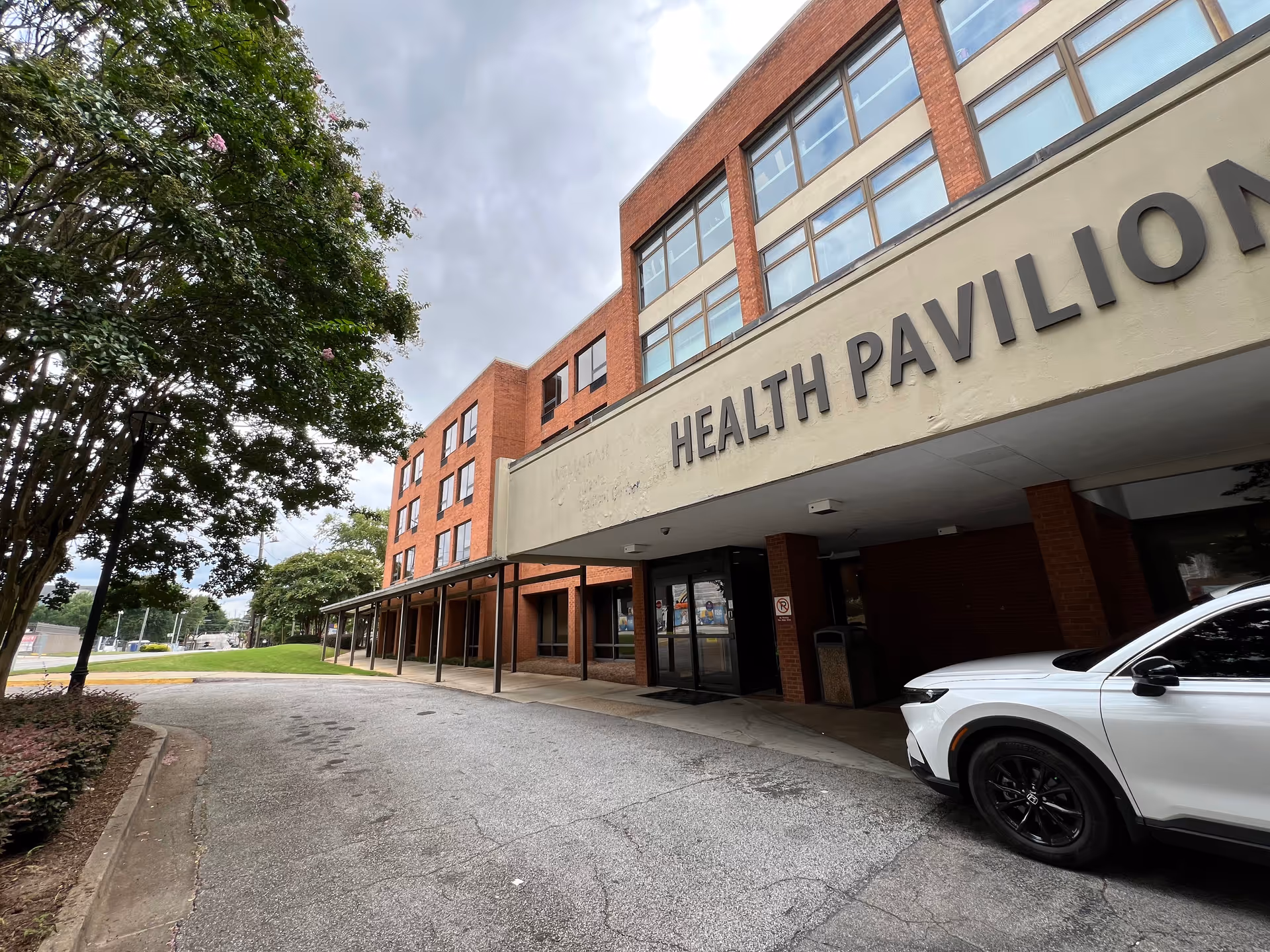 Exterior view of a brick health pavilion building with a covered entrance and a white SUV.