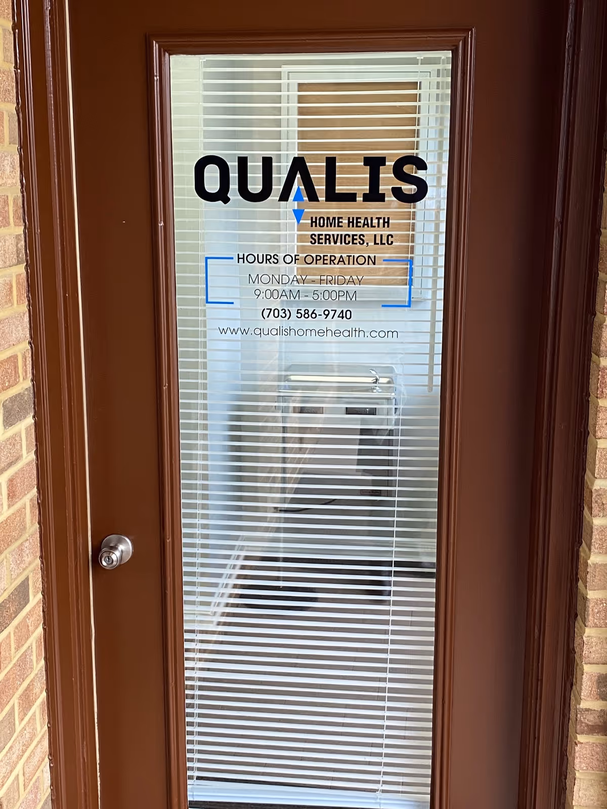 Glass door displays Qualis Home Health Services logo and hours through blinds.