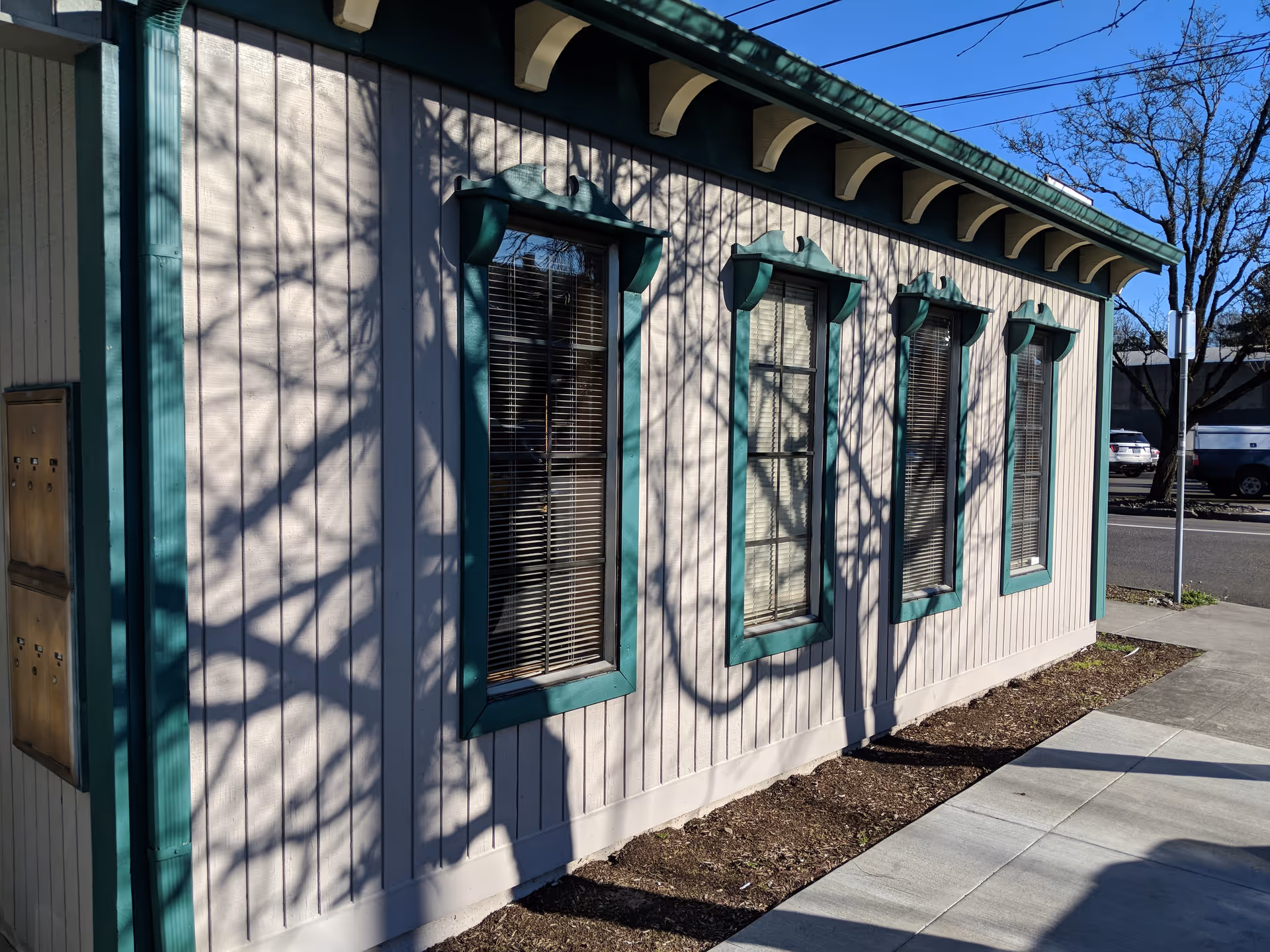 Exterior view of a small beige building with teal trim and multiple windows.