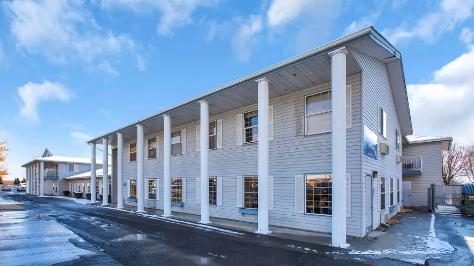 Two-story light gray senior living building with white columns and windows.