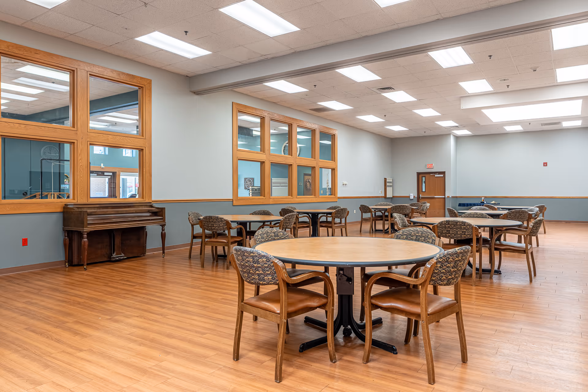 Round tables with chairs arranged in a spacious dining area with wood flooring.
