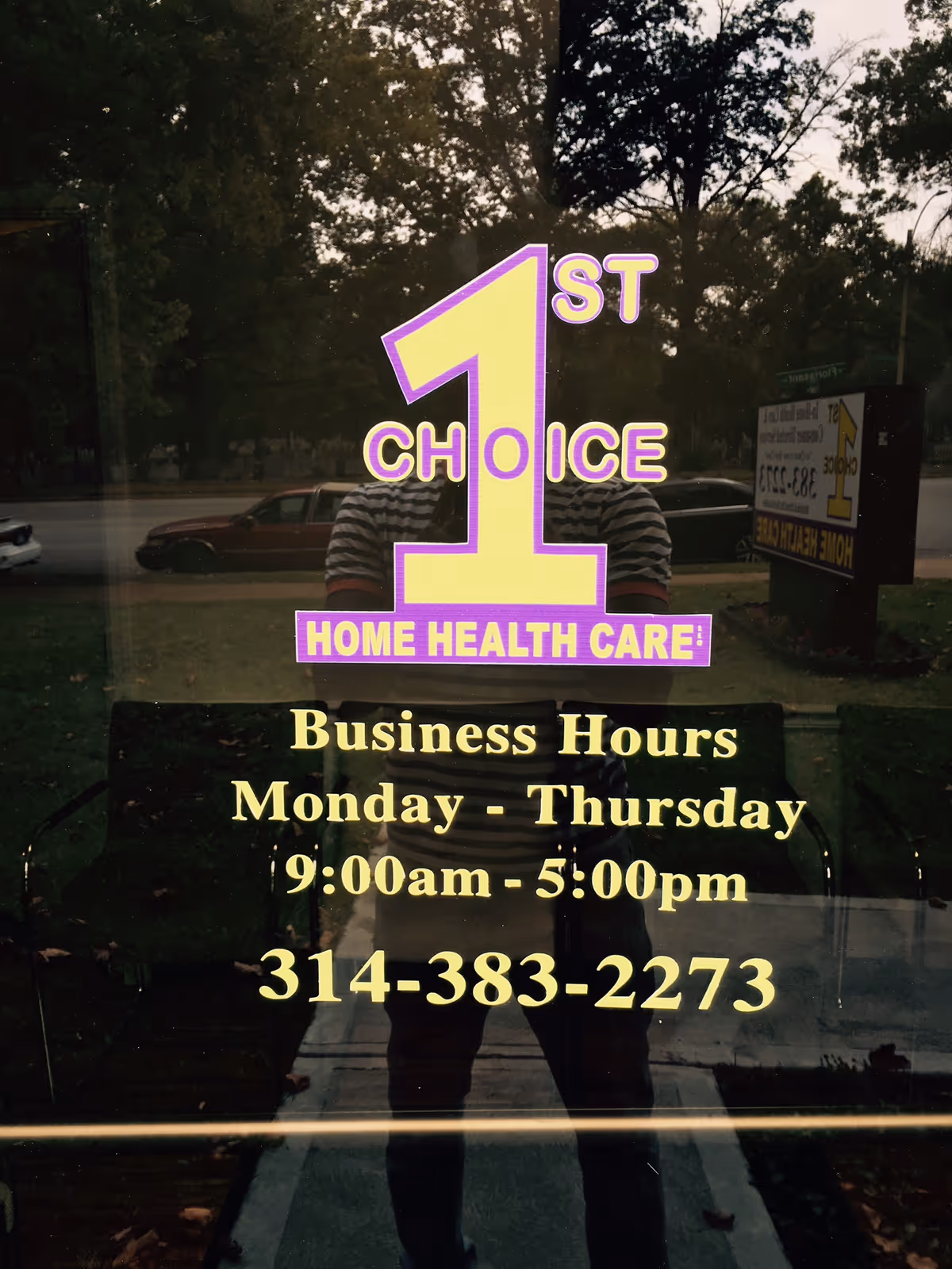 Reflective glass storefront displaying yellow and purple 1st Choice Home Health Care sign and hours.