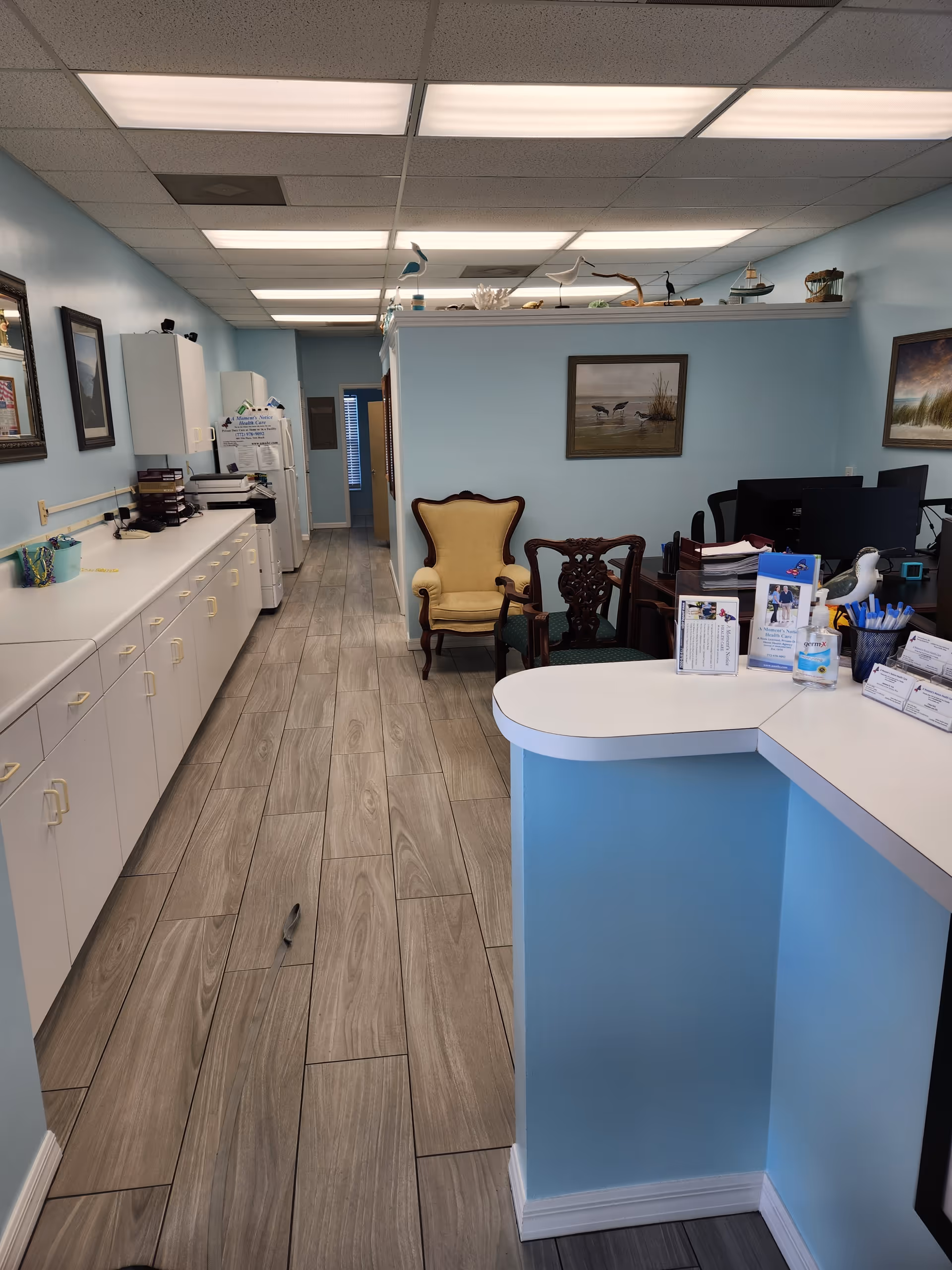 Reception area featuring curved blue counter, light-blue walls, long white cabinets, and seating at the back.