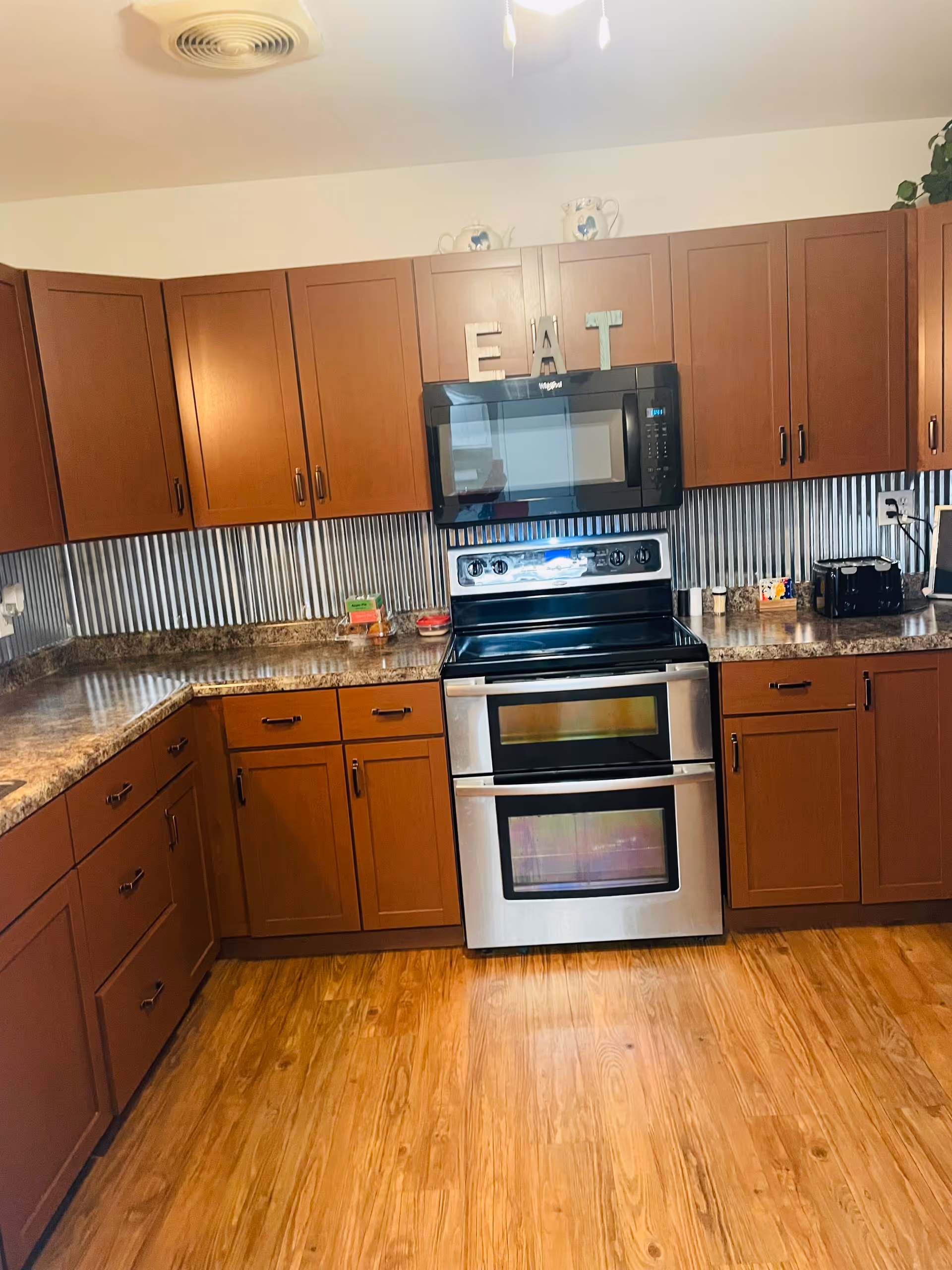 U-shaped kitchen with wooden cabinets, stainless stove, microwave, granite counters, and 'EAT' letters