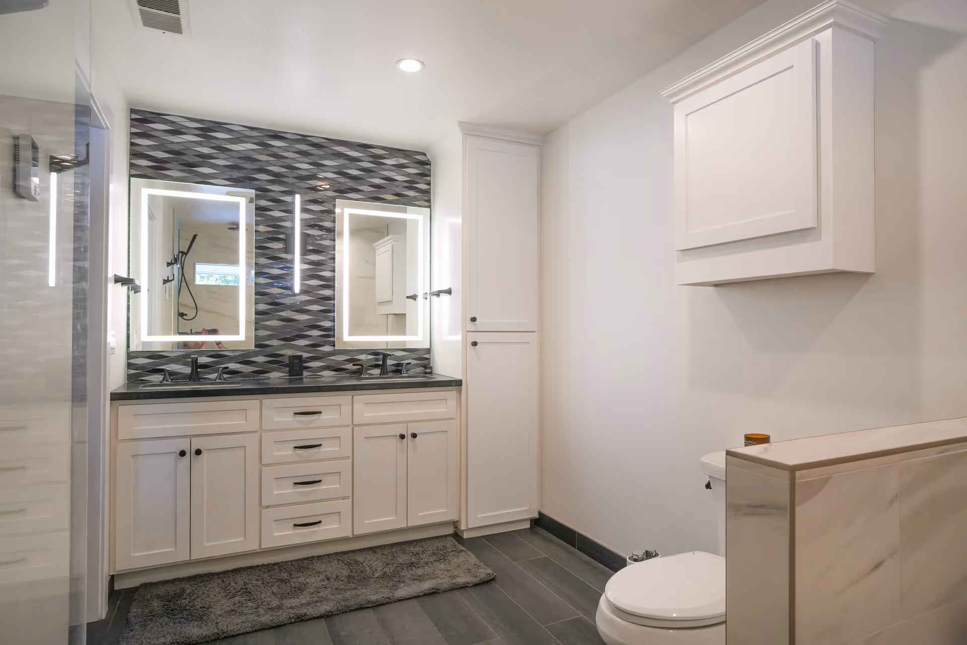 Bright bathroom in Fernwood Care Facility with double vanity, backlit mirrors, and a toilet.
