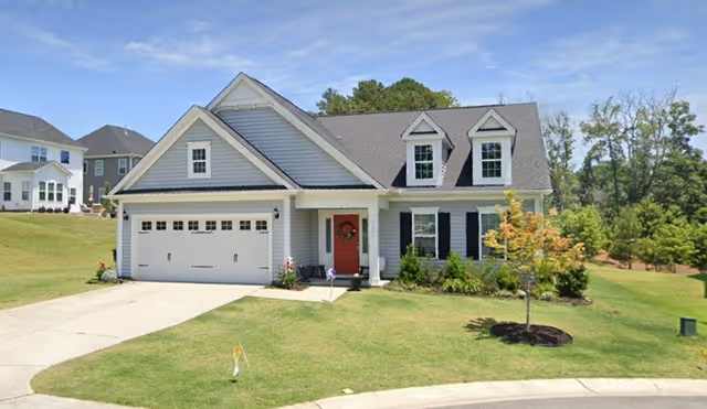 Front exterior of a two-story care home with a two-car garage and red front door.