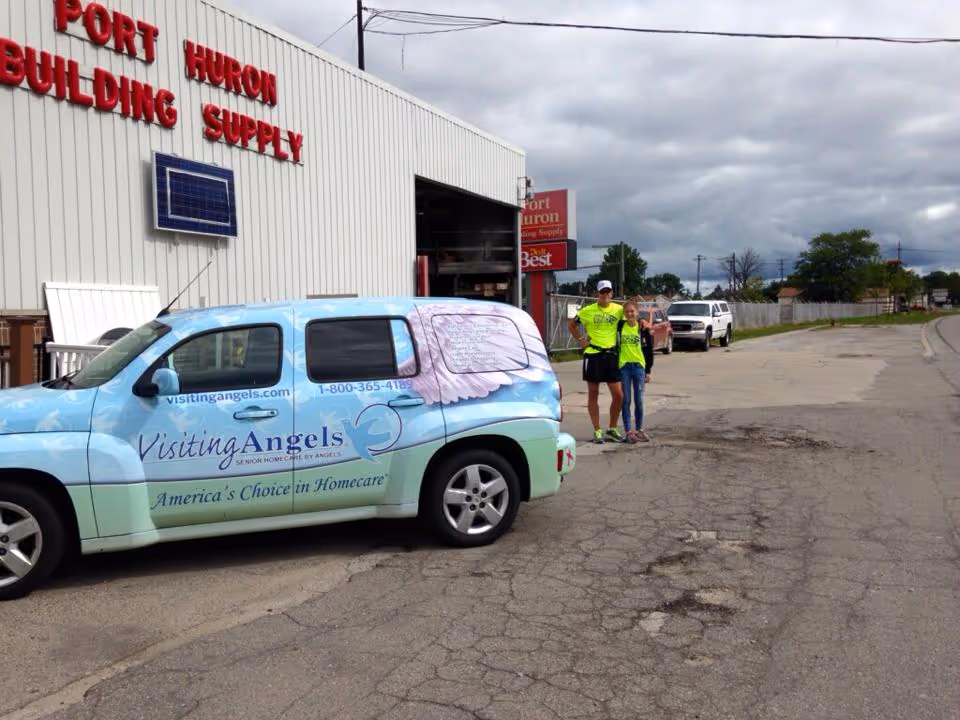 Colorful Visiting Angels van parked beside a building with two staff nearby.
