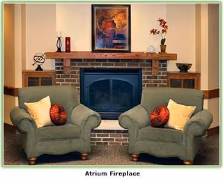 Two green armchairs flank a brick fireplace in a cozy atrium living room.