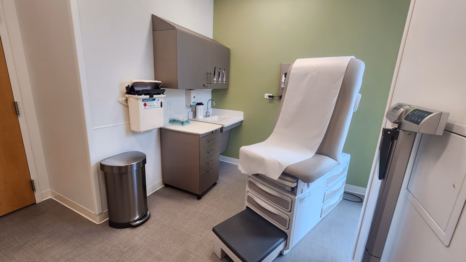 Examination room with a medical chair, sink, cabinets, and a weighing scale.