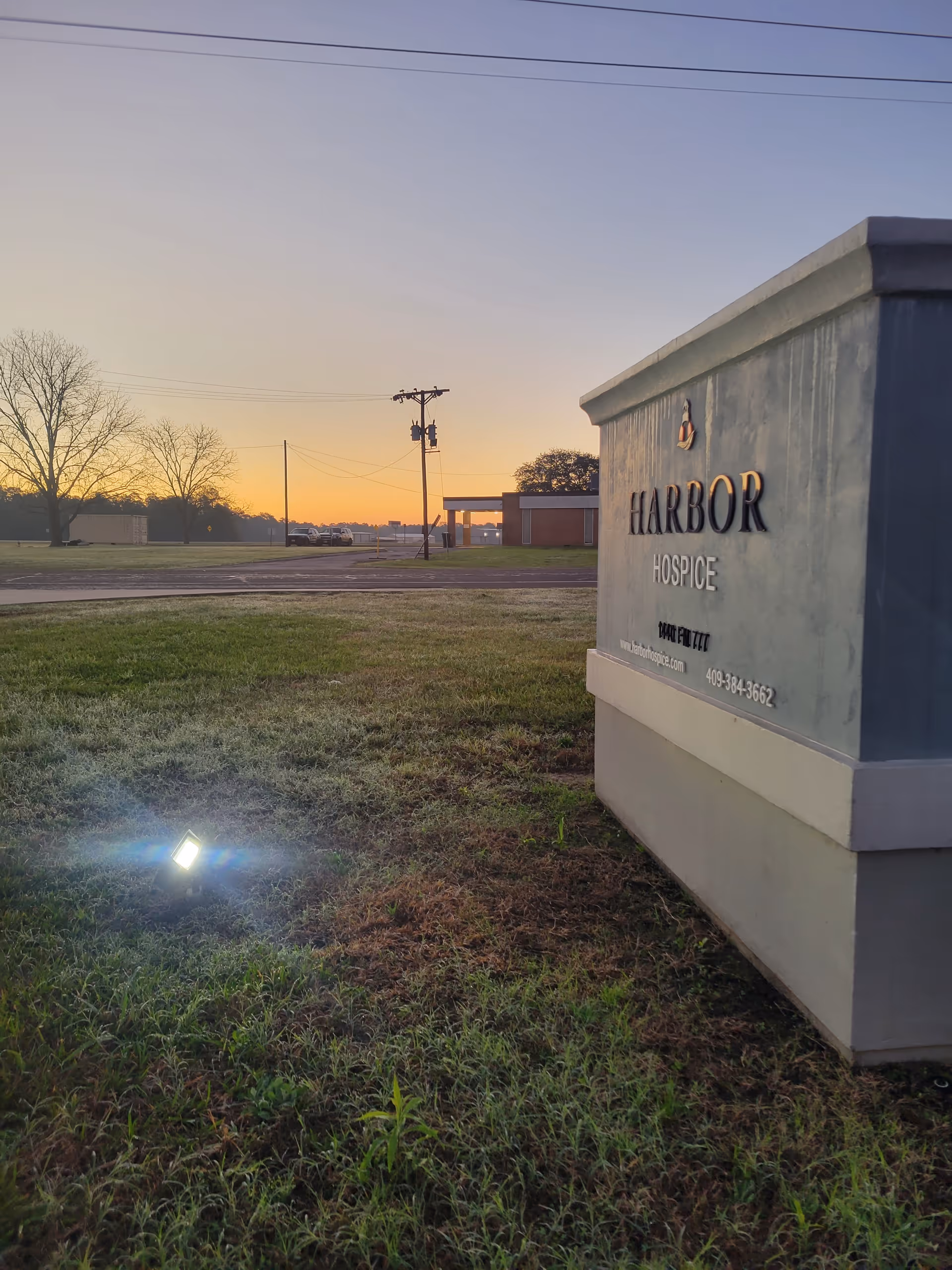 Sunset over a grassy area with a Harbor Hospice sign in foreground.