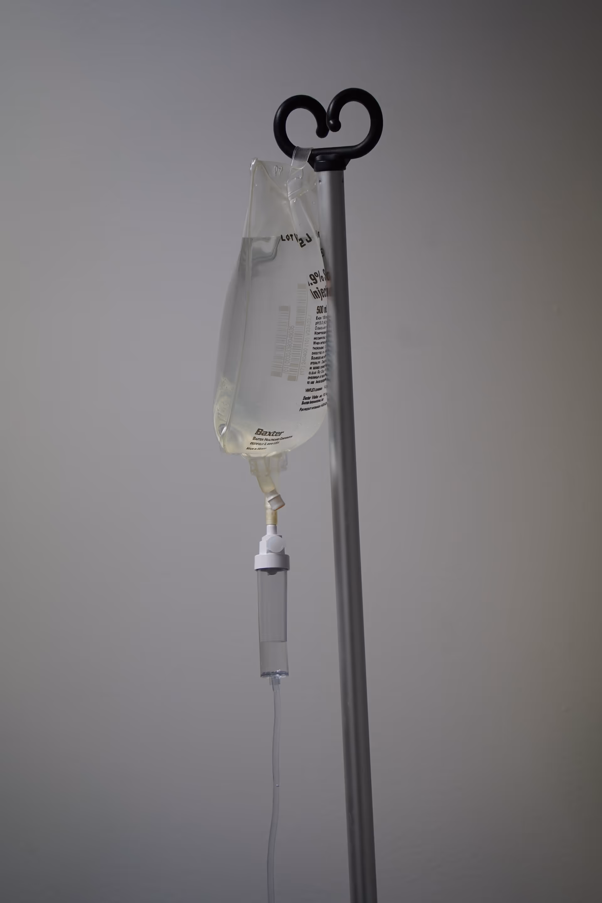 IV drip bag is suspended on a pole in a plain medical room.