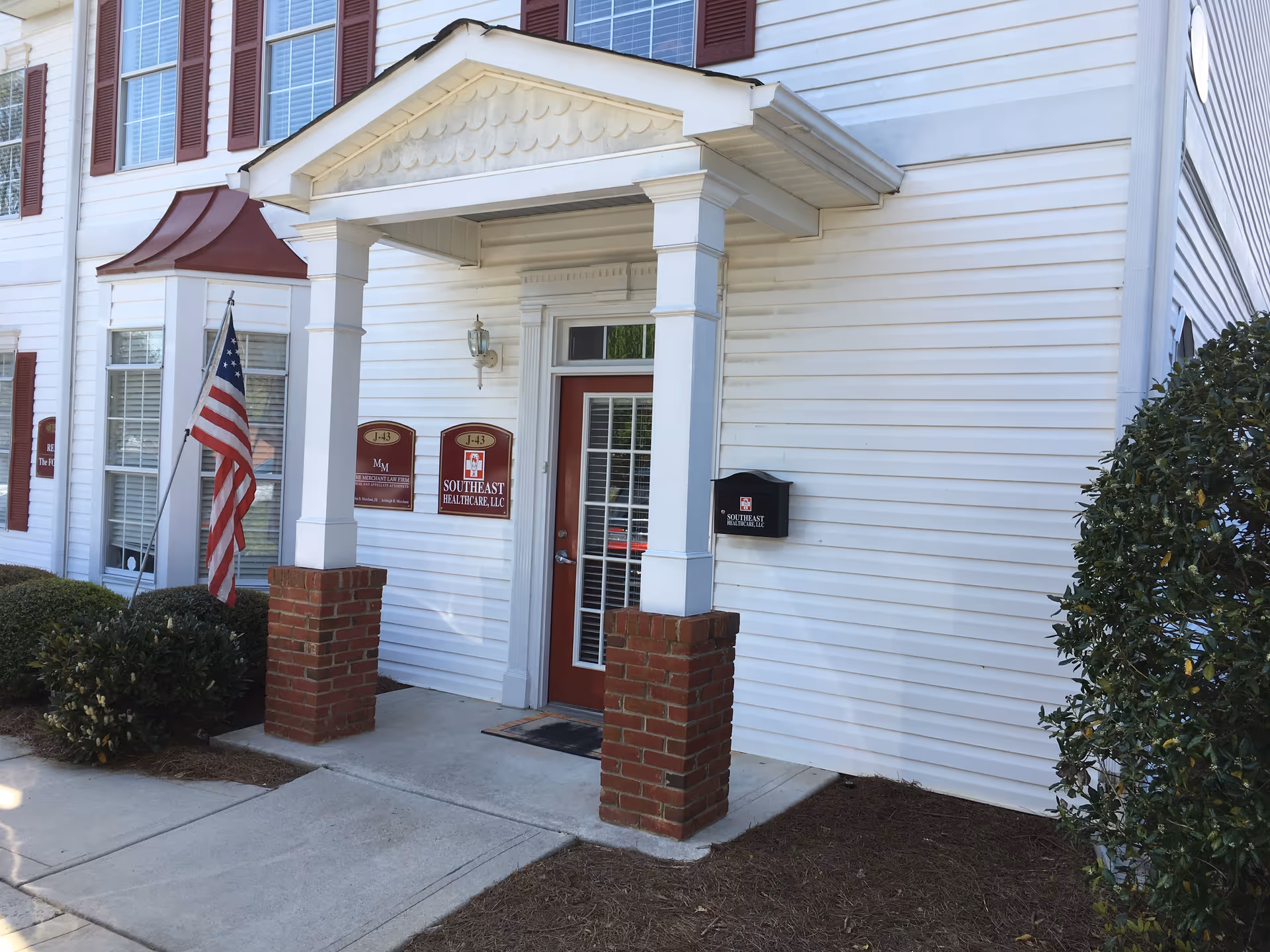 White siding building exterior with front entrance, brick columns, American flag, and Southeast Healthcare signage.