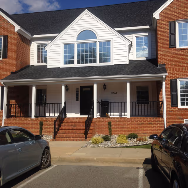 Front exterior of a brick senior living facility with a covered porch and parked cars.