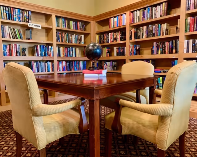 Library reading area with wooden table, four chairs, globe, and tall bookshelves.