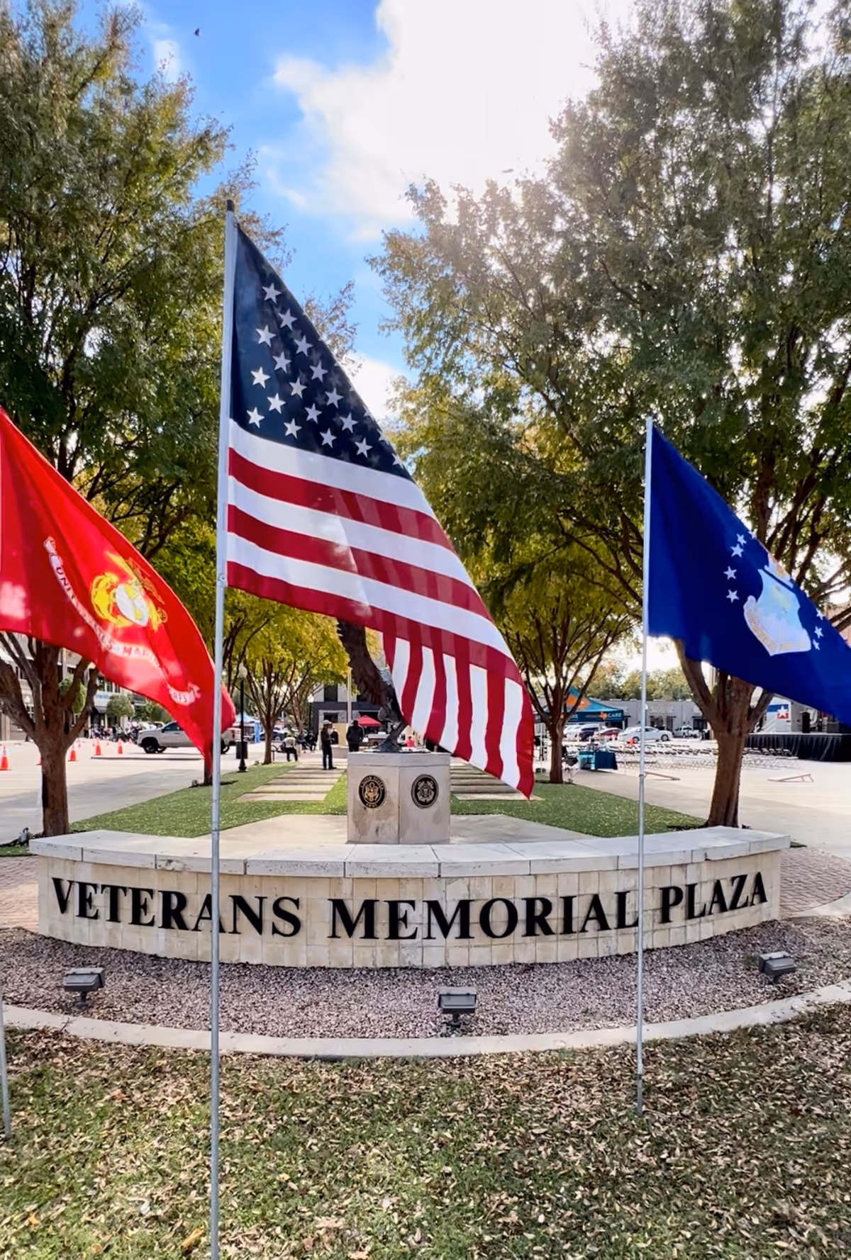 Outdoor Veterans Memorial Plaza with flags and a curved stone inscription.