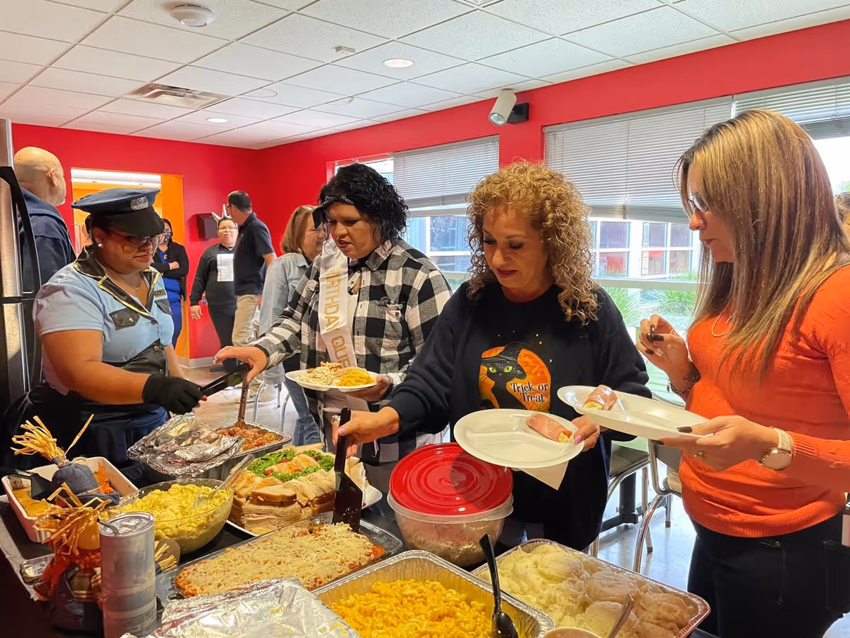 People line up at a buffet in a bright red-walled dining room.