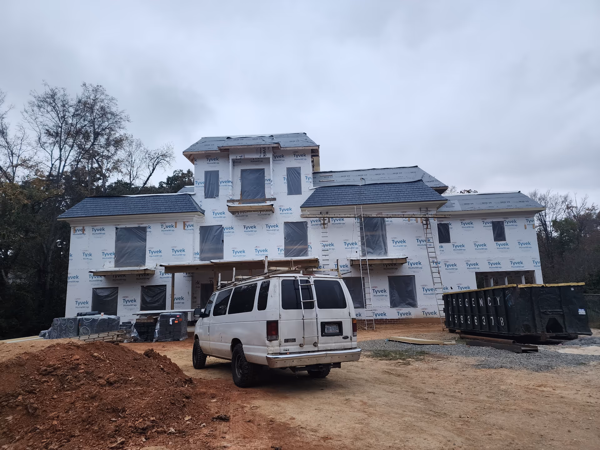 A multi-story house under construction wrapped in Tyvek with a white van parked at the front.