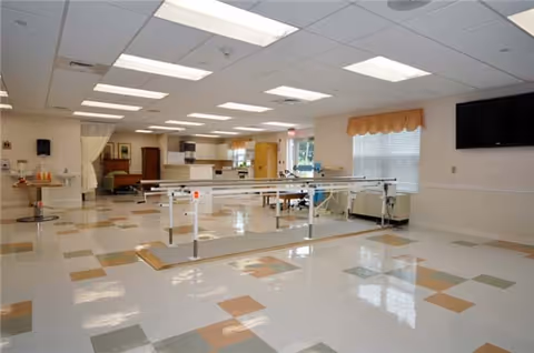 A spacious rehab area inside a senior care facility with parallel bars and equipment.