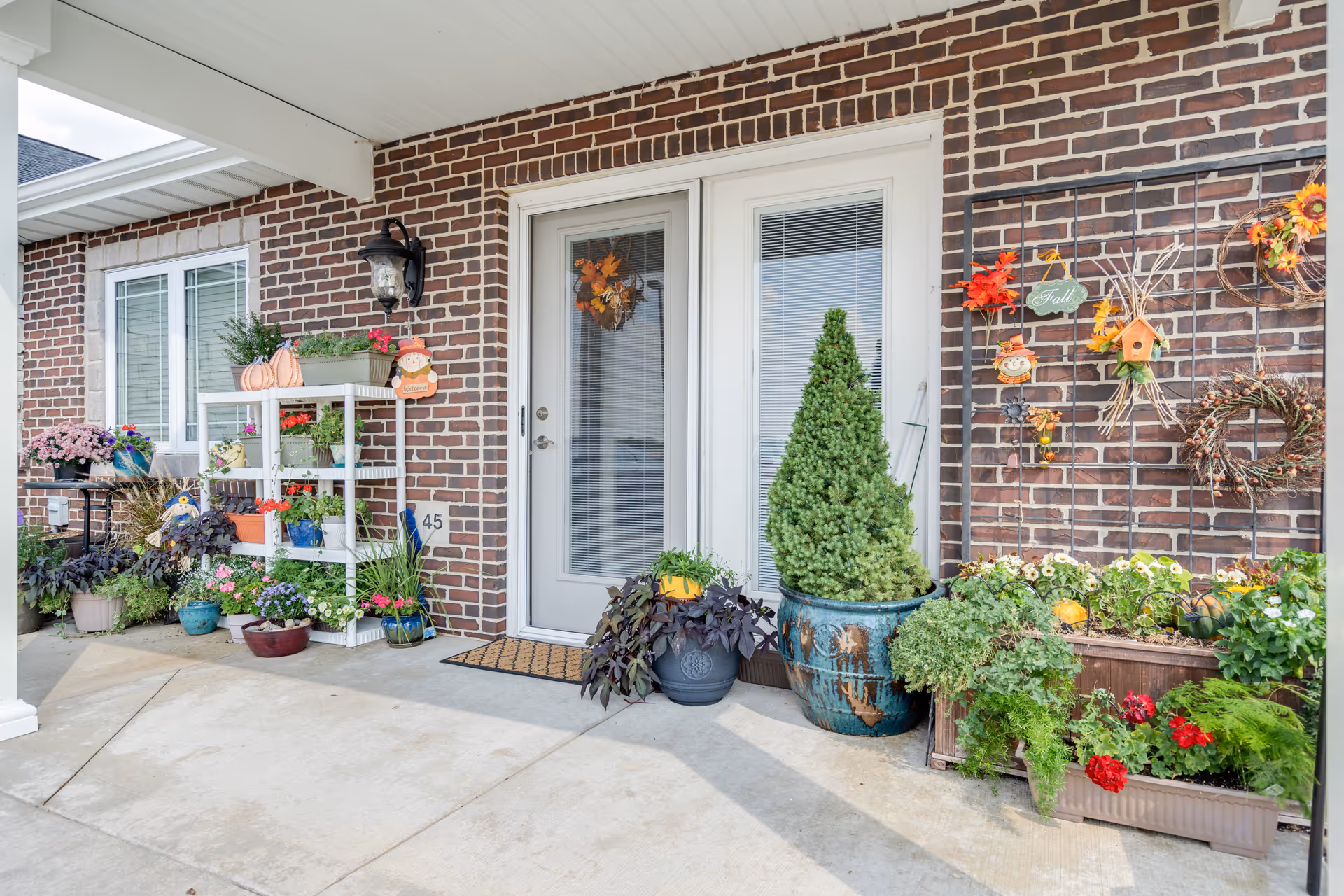 Brick building front entrance with door, porch planters, and fall-themed decorations.