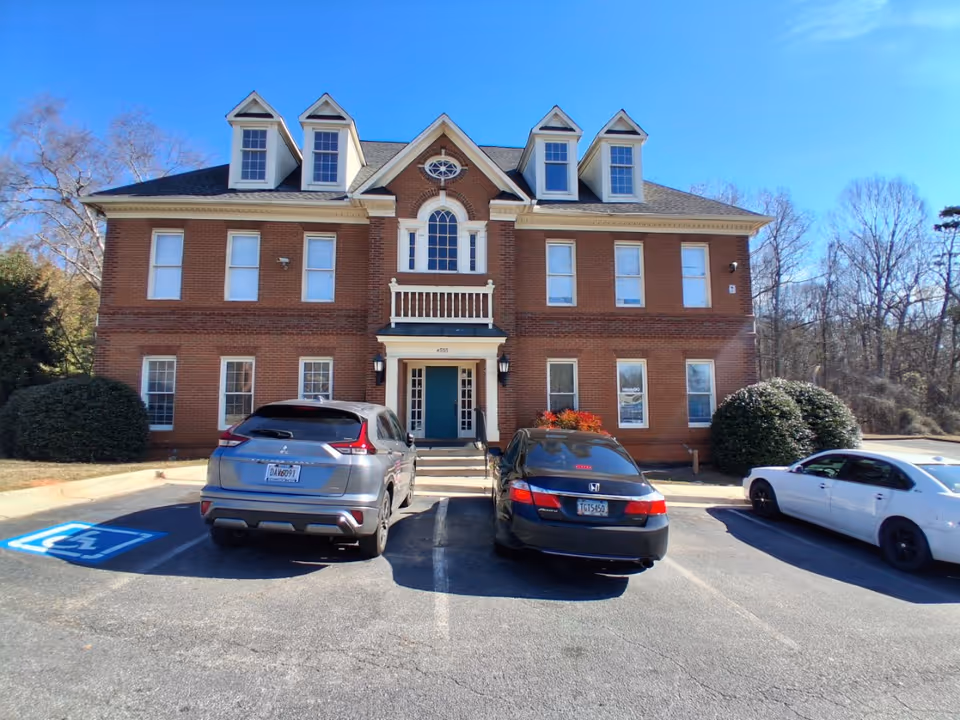 Brick senior living facility exterior with parked cars in front and leafless trees.