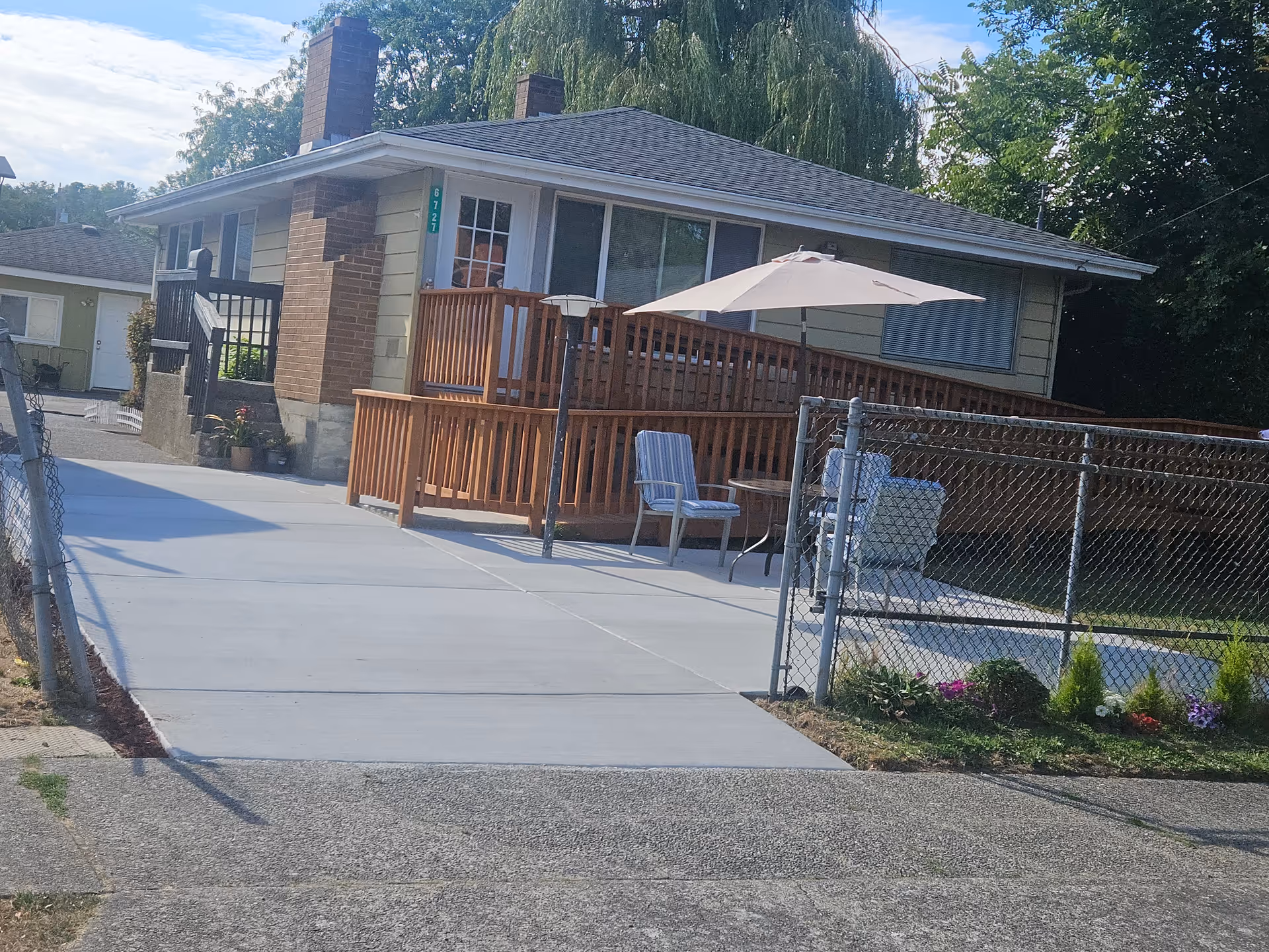 Single-story residential facility exterior with wooden deck, patio umbrella, seating, and chain-link fence.