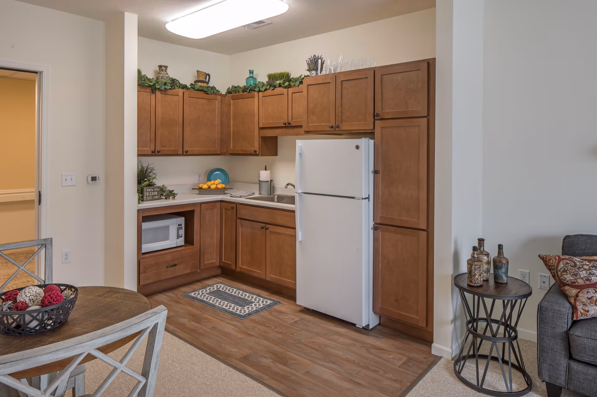 An L-shaped kitchen with wooden cabinets, a white fridge, microwave, and adjoining dining area.
