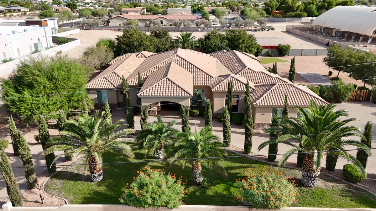 A single-story senior living facility with a tile roof, palms, and manicured landscaping at the front.