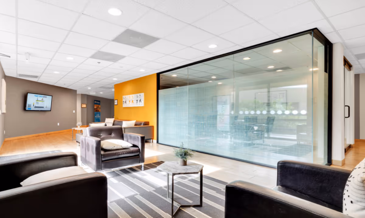 Modern senior living facility lounge with black couches, glass partition, orange accent wall, and coffee table.