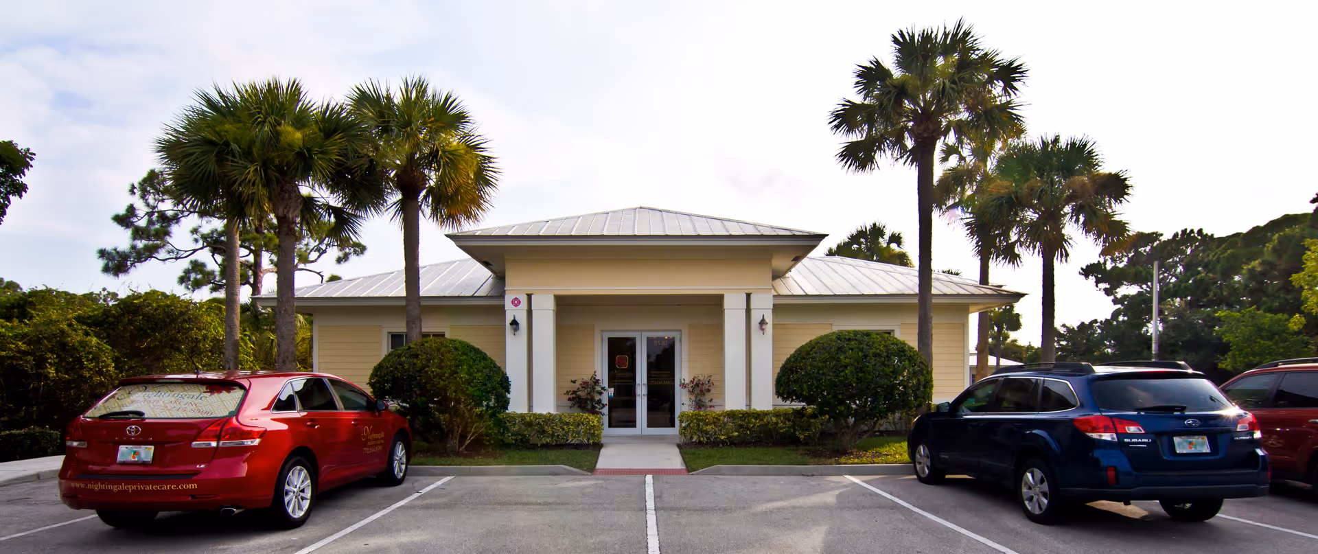 Front view of a pale facility with entrance, palm trees, and parked cars.