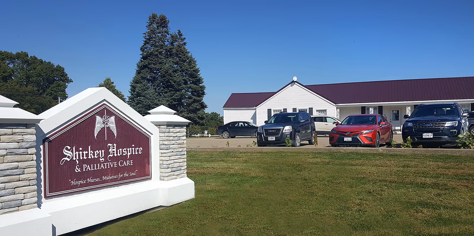 Shirkey Hospice sign in foreground with facility exterior and parked cars.