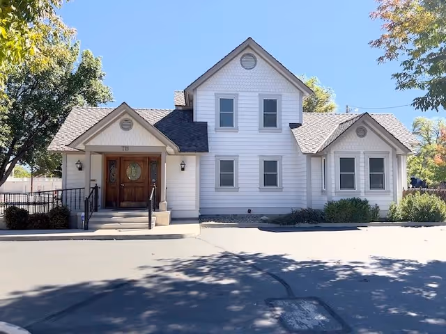 Front view of a white, two-story senior care facility with a wooden door and steps.
