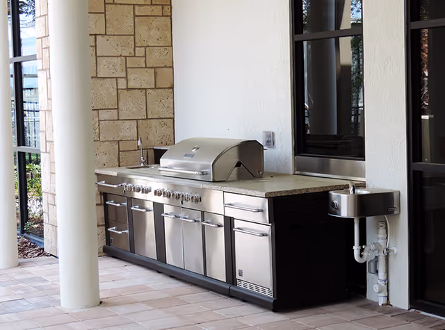 Outdoor stainless steel barbecue grill area with countertop, sink, and stone column on patio
