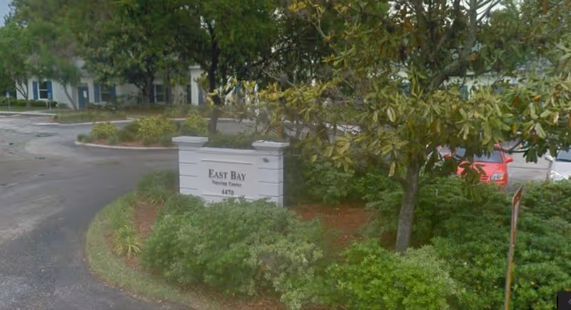 Exterior view of East Bay Nursing Center sign amid trees and shrubs.